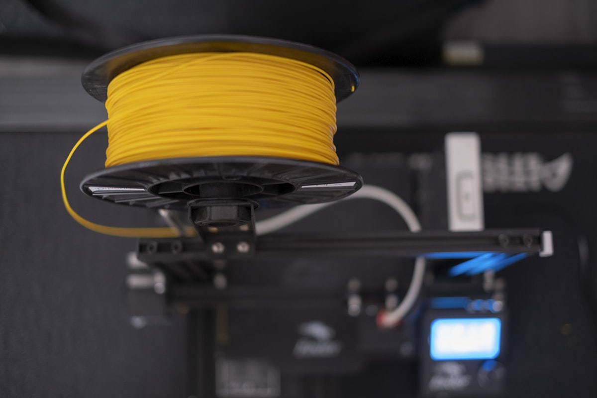 Yellow PLA filament spool mounted on 3D printer for Bambu A1 Mini printing